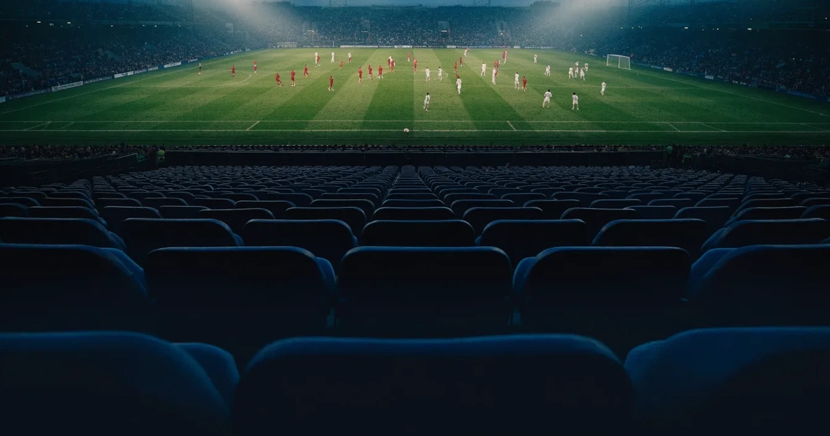 Leere Sitzreihen eines großen Stadions unter Flutlicht, dahinter die ferne Sicht auf den hell beleuchteten Rasen nach Sonnenuntergang.