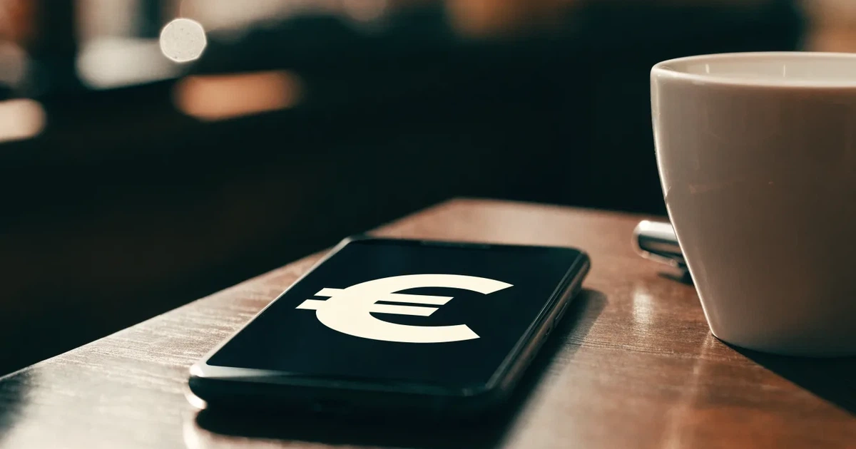 Ein Smartphone liegt mit dunklem Display auf einem Café-Tisch neben einer Tasse Kaffee und einem Kugelschreiber.