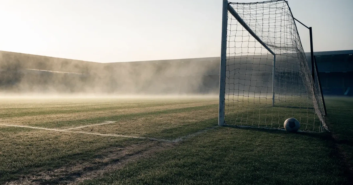 Ein Fußballtor mit Netz steht auf einem leeren Platz im Nebel der Morgendämmerung, der Rasen ist taufeucht.