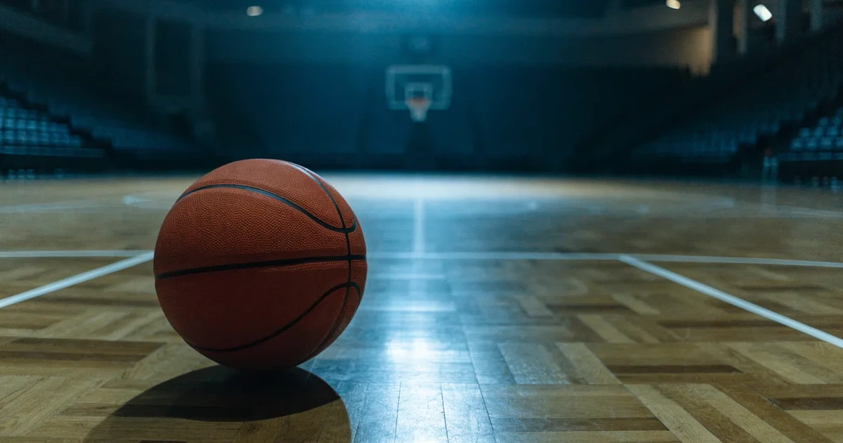 Ein Basketball liegt auf dem Parkettboden einer leeren Arena, Scheinwerfer werfen Licht auf die Mittellinie.