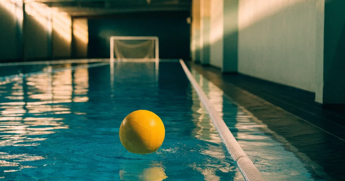 Ein Schwimmbecken mit türkisfarbenem Wasser und zwei schwimmenden Torrahmen am gegenüberliegenden Beckenrand, menschenleer unter Hallenlicht.