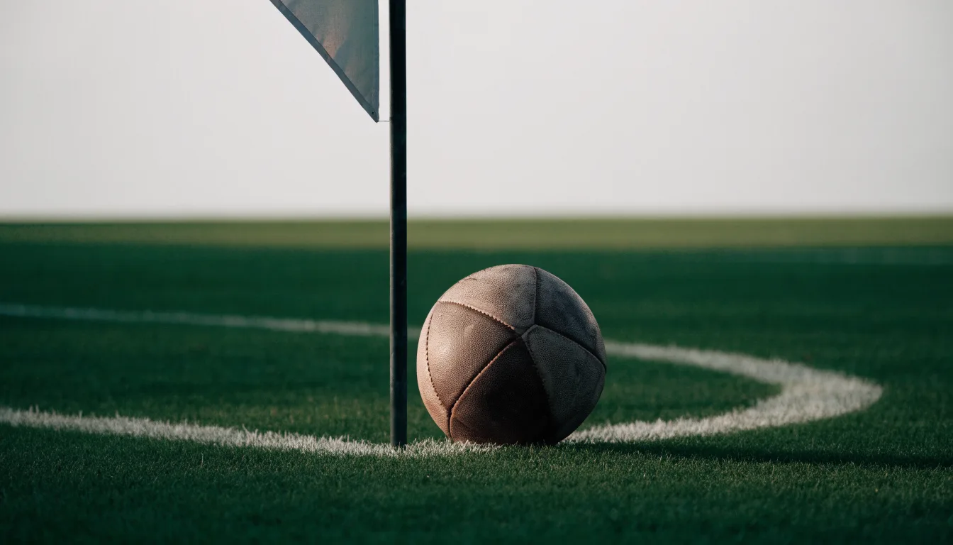 Ein Fußball liegt neben einer Eckfahne auf kurz gemähtem Rasen unter bewölktem Himmel.